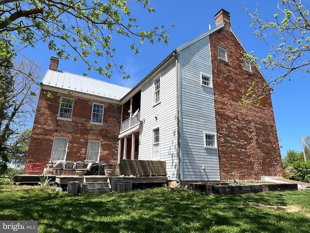 rear view of house featuring a chimney, a balcony, a lawn, and a deck