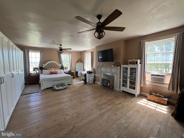 bedroom with wood-type flooring, multiple windows, cooling unit, and a fireplace with flush hearth