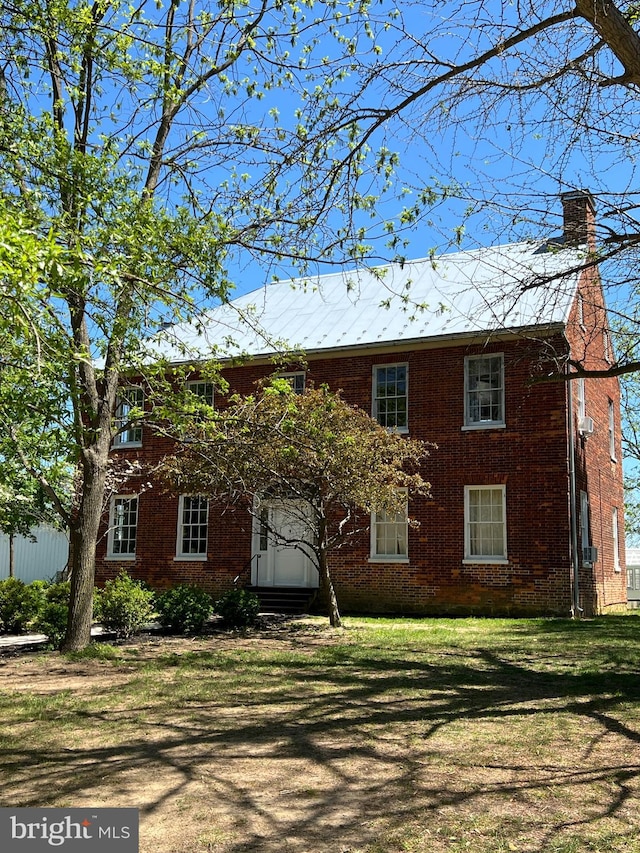colonial-style house featuring a chimney, brick siding, and a front lawn