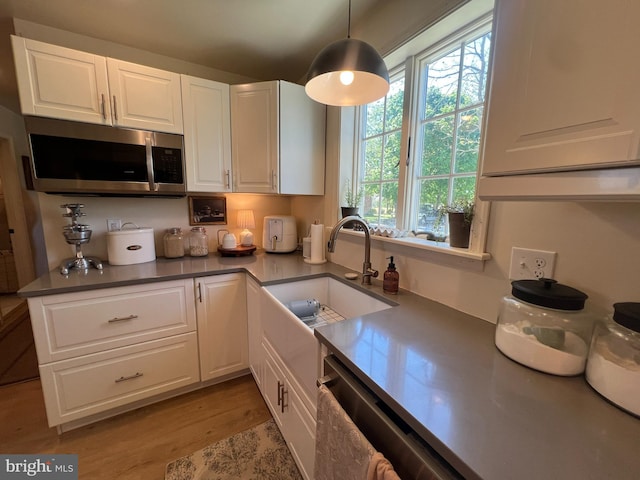 kitchen featuring stainless steel appliances, white cabinetry, a sink, light wood finished floors, and decorative light fixtures