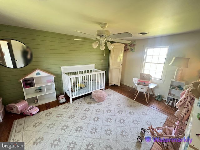 bedroom with a crib, wood walls, baseboards, and ceiling fan