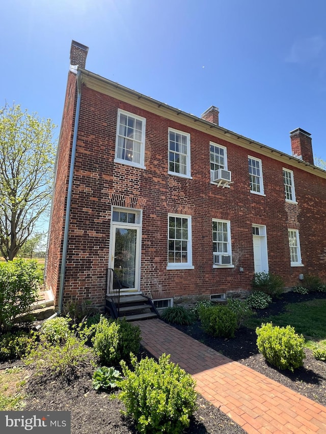 view of front of property featuring a chimney, brick siding, and cooling unit