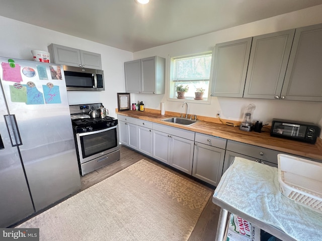 kitchen featuring stainless steel appliances, gray cabinetry, a sink, wooden counters, and wood finished floors