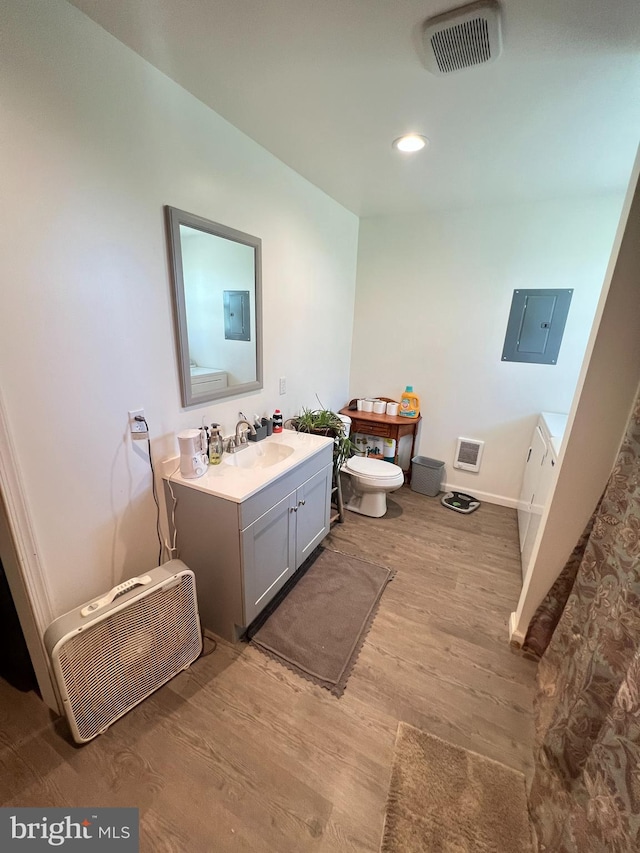 bathroom with electric panel, wood finished floors, toilet, vanity, and baseboards