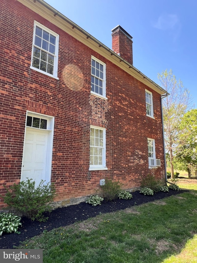 view of home's exterior featuring a chimney, brick siding, a lawn, and cooling unit