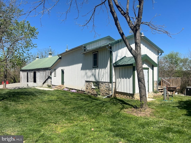 rear view of property featuring board and batten siding, a lawn, and a wooden deck