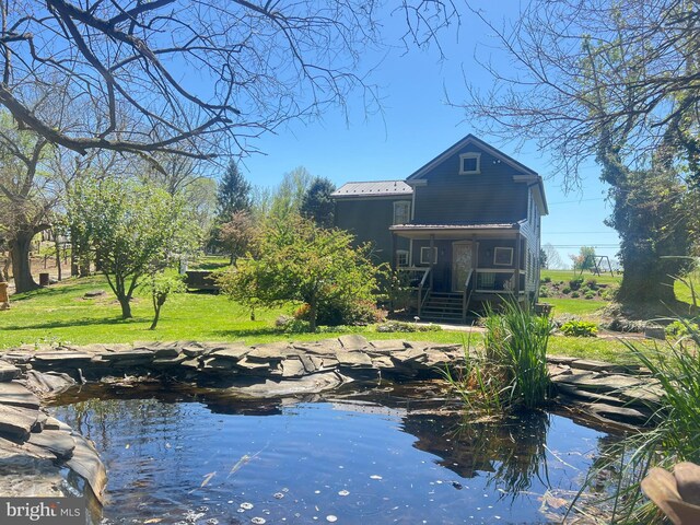 back of house featuring a lawn, a garden pond, and covered porch