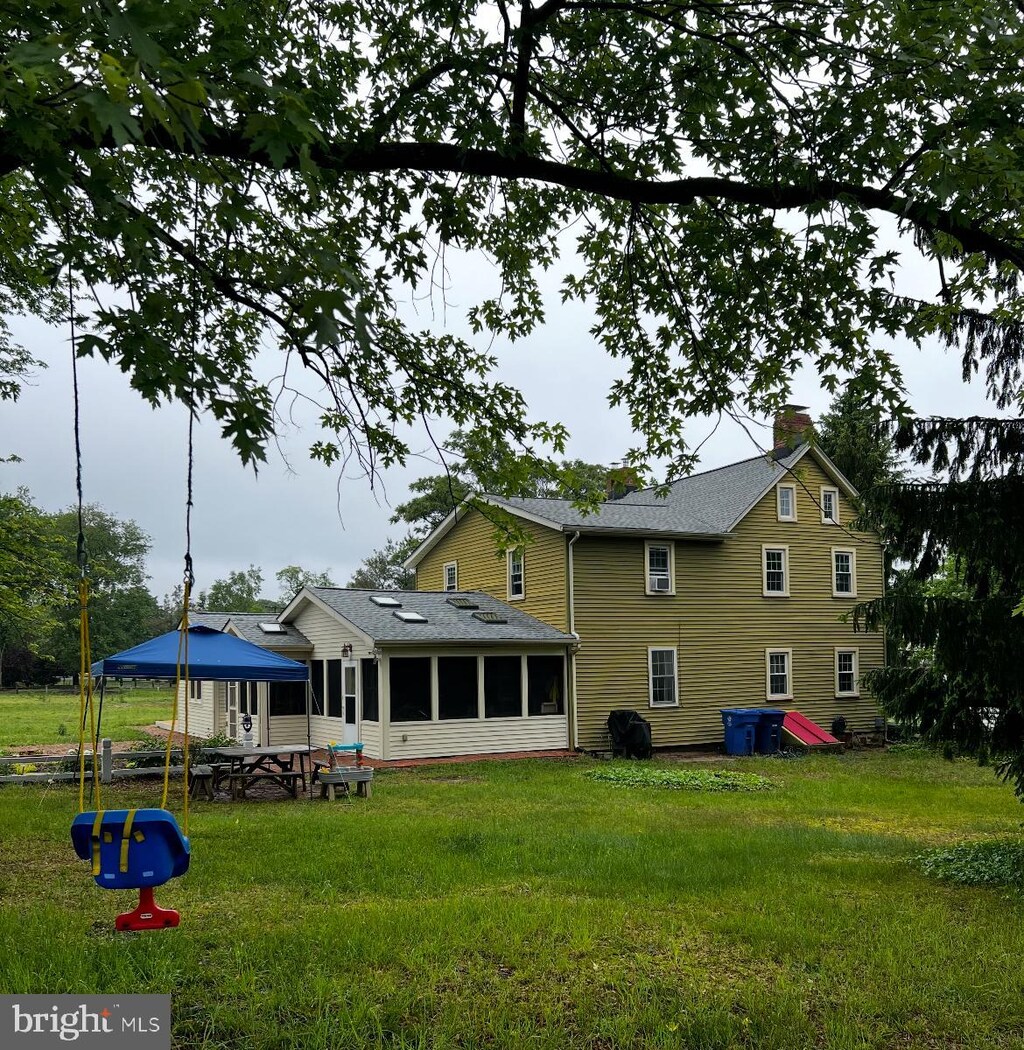 back of house with a chimney, a sunroom, a yard, a gazebo, and a shingled roof