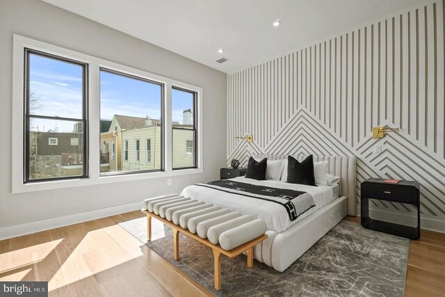 bedroom featuring an accent wall, baseboards, wood finished floors, and recessed lighting