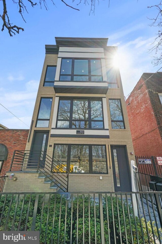 view of front of house featuring brick siding, a balcony, and fence