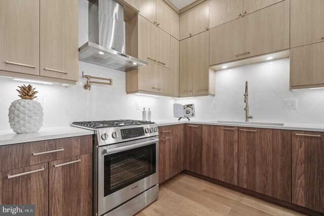 kitchen with wall chimney exhaust hood, stainless steel range with gas stovetop, a sink, and light countertops