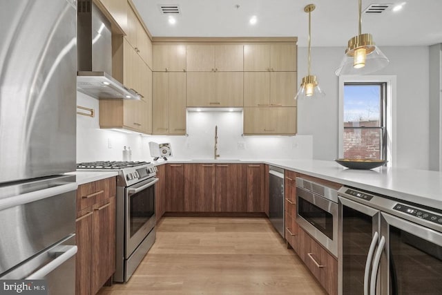 kitchen with appliances with stainless steel finishes, wall chimney exhaust hood, a sink, light countertops, and pendant lighting