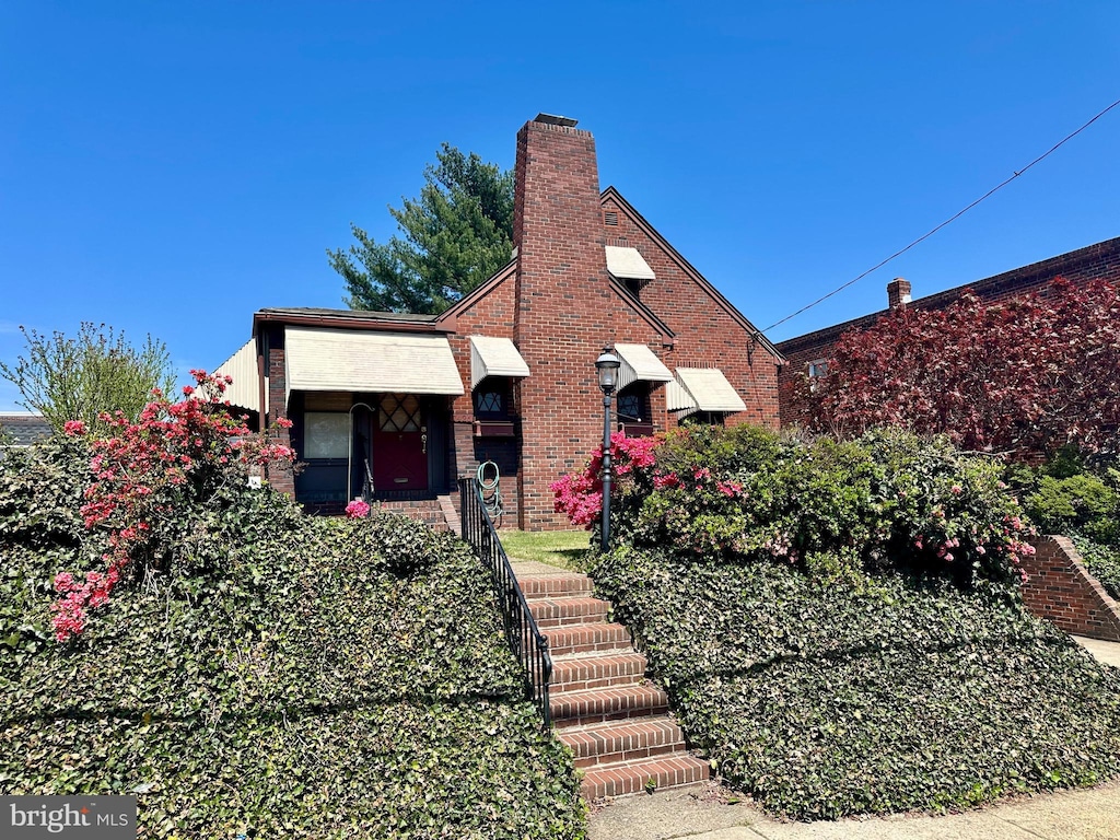 english style home featuring brick siding and a chimney