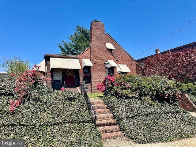 english style home featuring brick siding and a chimney