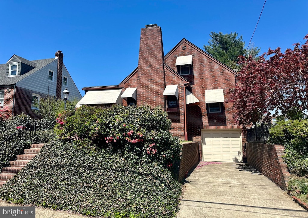 tudor house featuring brick siding, concrete driveway, an attached garage, and a chimney