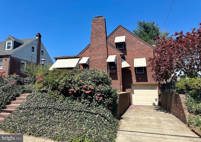 tudor house featuring brick siding, concrete driveway, an attached garage, and a chimney