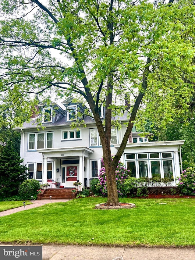american foursquare style home featuring a front lawn, a porch, and stucco siding
