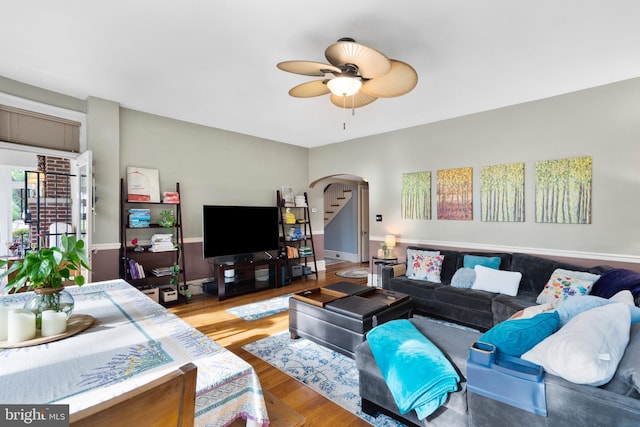 living area with arched walkways, ceiling fan, and wood finished floors