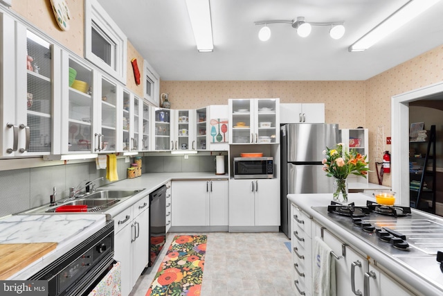 kitchen with stainless steel appliances, wallpapered walls, a sink, white cabinets, and light countertops