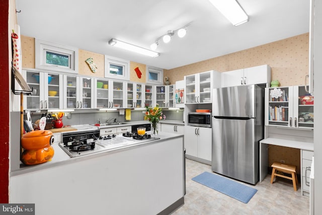kitchen featuring stainless steel appliances, white cabinetry, a sink, glass insert cabinets, and wallpapered walls