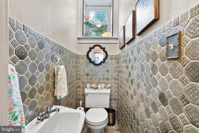 half bathroom with a sink, toilet, and tile walls