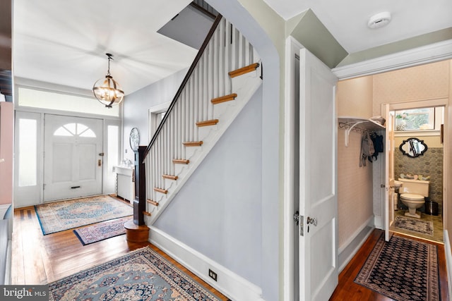 entrance foyer with wood finished floors, stairway, a chandelier, arched walkways, and baseboards