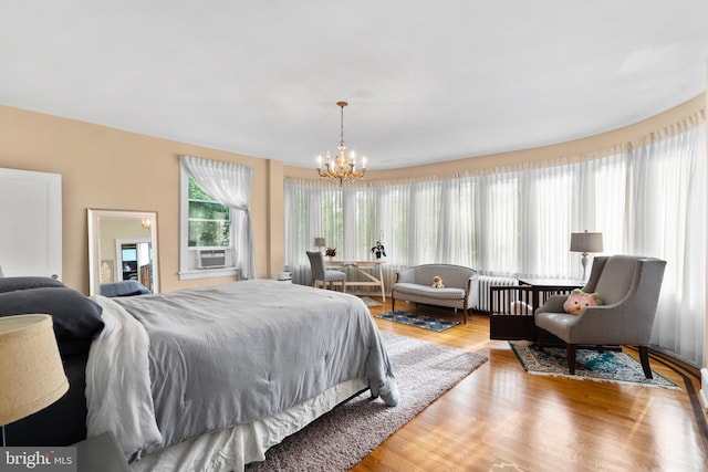 bedroom featuring a chandelier, wood finished floors, radiator heating unit, and cooling unit