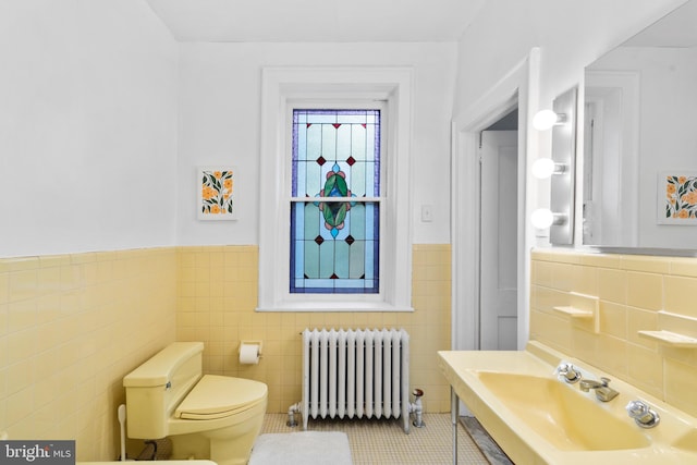 bathroom featuring radiator heating unit, tile walls, a sink, tile patterned flooring, and a wainscoted wall