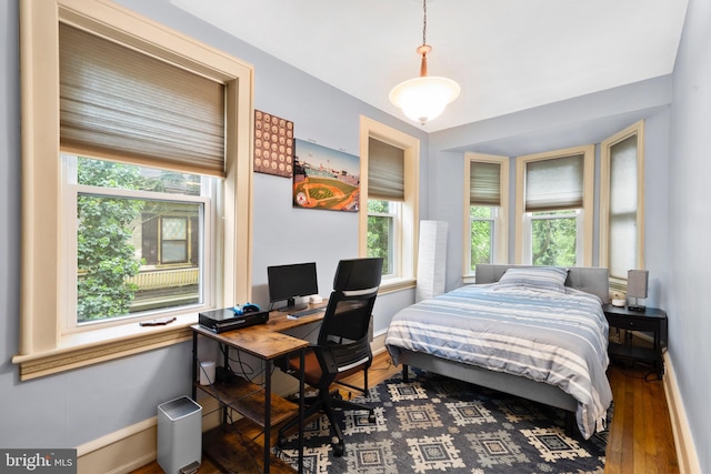 bedroom featuring baseboards, multiple windows, wood finished floors, and a desk