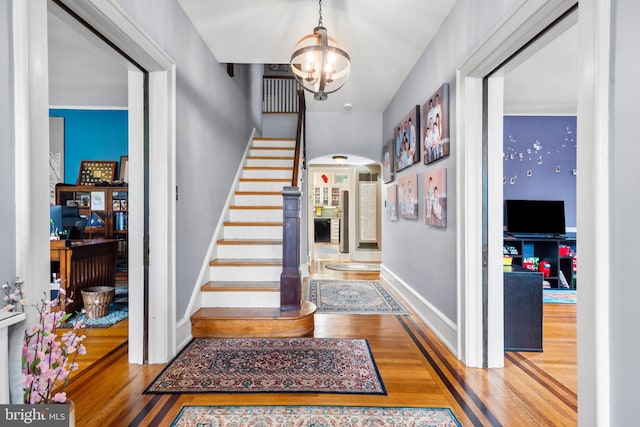 foyer entrance with arched walkways, wood finished floors, stairway, and baseboards