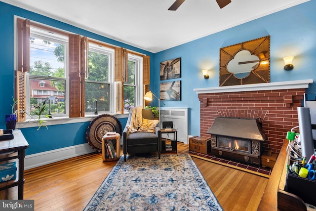 living area with wood finished floors, a ceiling fan, crown molding, and baseboards