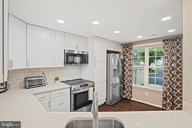 kitchen with appliances with stainless steel finishes, dark wood-style floors, white cabinets, a sink, and recessed lighting