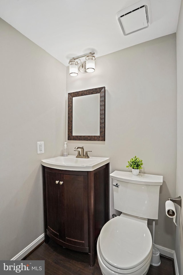 half bath with baseboards, vanity, wood finished floors, and toilet