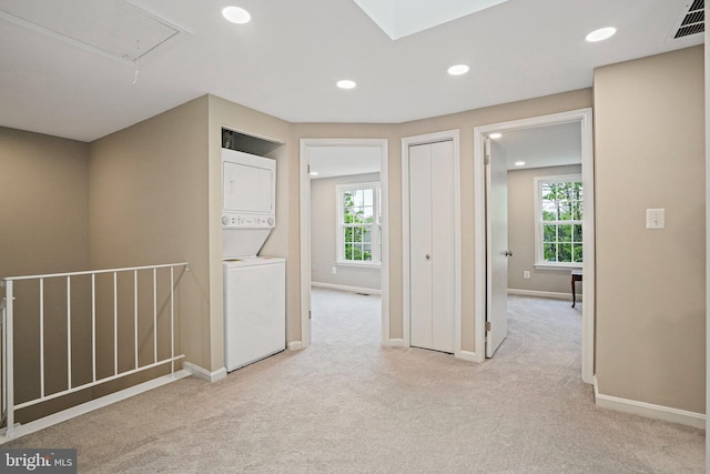 hall with stacked washing machine and dryer, attic access, healthy amount of natural light, light carpet, and recessed lighting