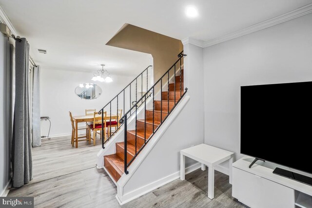 stairs with wood finished floors, a chandelier, ornamental molding, and baseboards