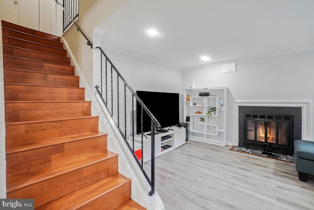 staircase featuring crown molding, wood finished floors, a fireplace with flush hearth, and recessed lighting