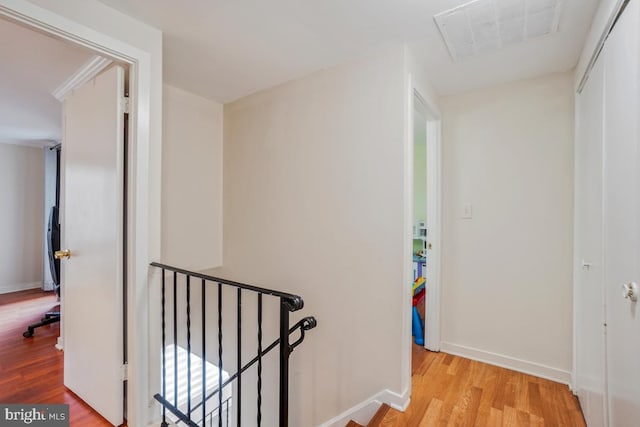 hallway with an upstairs landing, wood finished floors, and baseboards