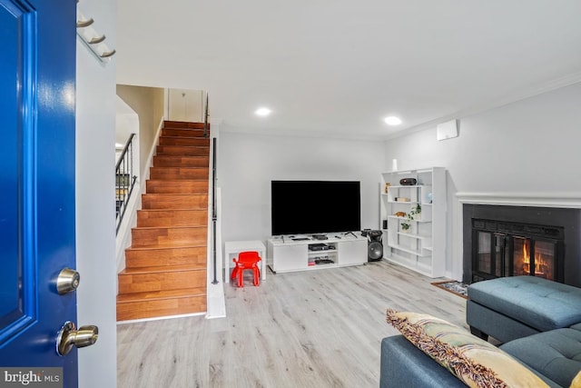 living area featuring stairway, wood finished floors, ornamental molding, a glass covered fireplace, and recessed lighting