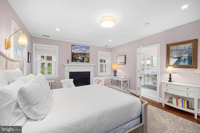 bedroom featuring radiator, wood finished floors, baseboards, a fireplace, and recessed lighting