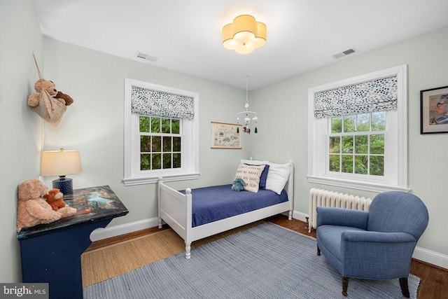 bedroom with radiator heating unit, baseboards, and wood finished floors