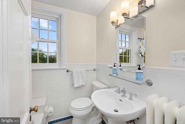 bathroom with tile walls, a sink, toilet, plenty of natural light, and a wainscoted wall