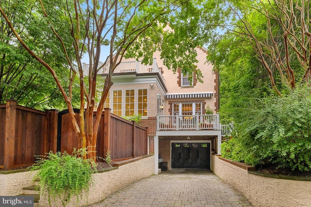 rear view of house featuring brick siding, decorative driveway, fence, stucco siding, and an attached garage