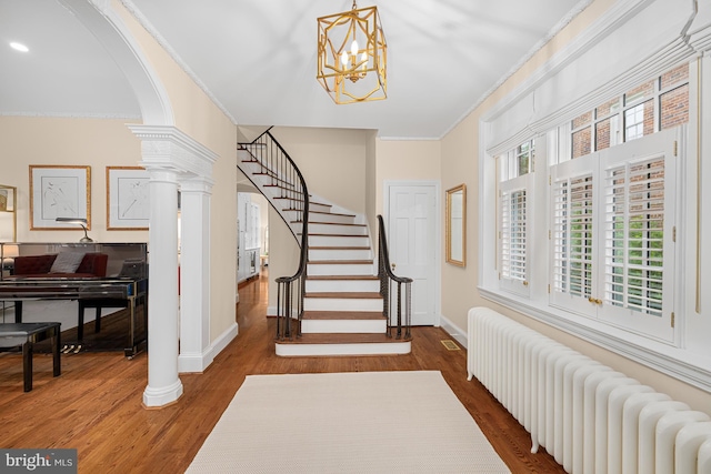 foyer featuring radiator heating unit, ornamental molding, wood finished floors, baseboards, and arched walkways