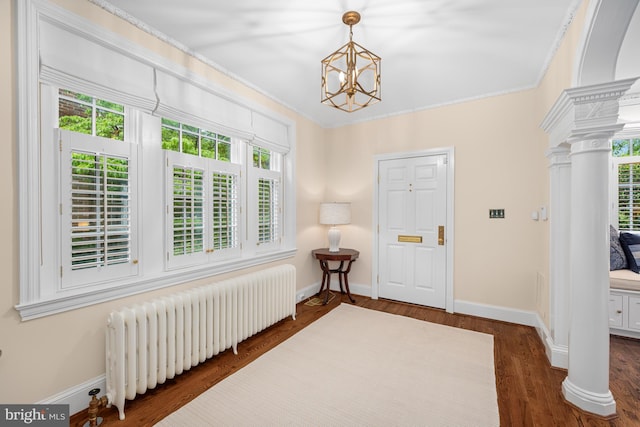 foyer featuring radiator heating unit, decorative columns, plenty of natural light, a chandelier, and ornamental molding