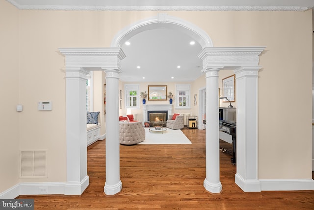 living room with a lit fireplace, wood finished floors, recessed lighting, baseboards, and ornate columns