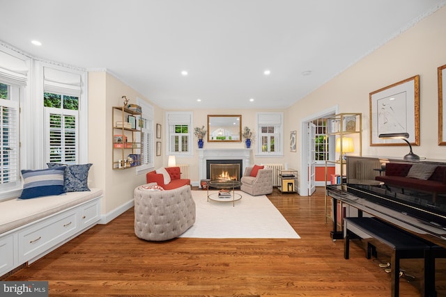 living room with wood finished floors, a lit fireplace, recessed lighting, radiator, and baseboards