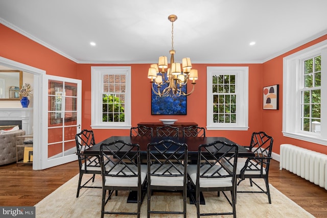 dining space with radiator, a chandelier, wood finished floors, ornamental molding, and baseboards