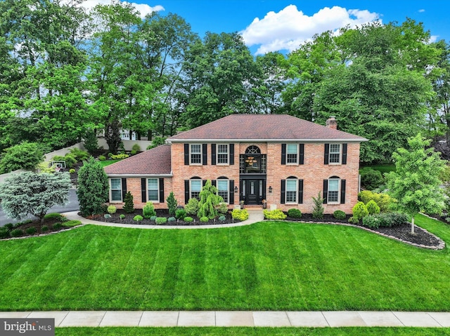 view of front of house with a chimney, a front lawn, brick siding, and a shingled roof
