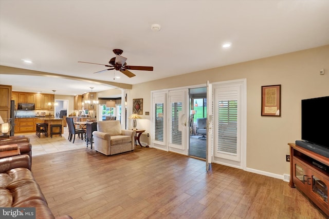 living room featuring a ceiling fan, light wood-style floors, baseboards, recessed lighting, and a chandelier