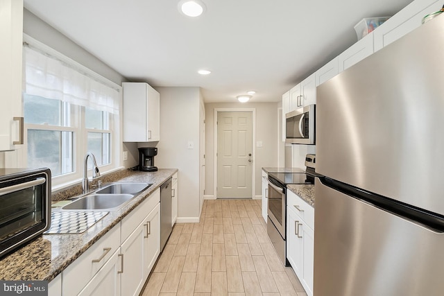 kitchen with stainless steel appliances, a sink, white cabinetry, baseboards, and light stone counters